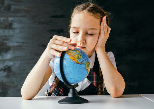 Little schoolgirl studies a globe at her desk against the background of a chalkboard.