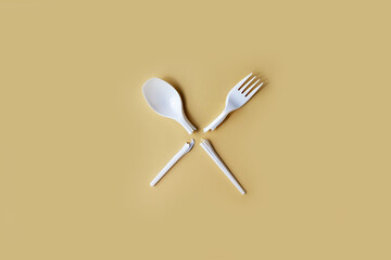 Broken disposable plastic fork and spoon on a uniform background.