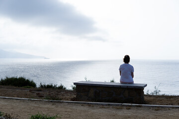 Woman sitting on a stone bench looking at the horizon on a sad and cloudy day