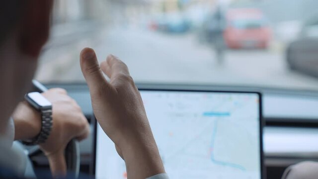 Successful businessman driving along the downtown street on high tech electric Tesla car Model 3 with male colleague nearby, man steering wheel, talking with friend, gesturing with hand on background