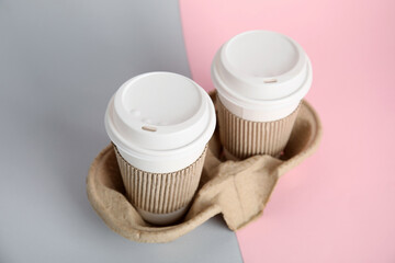 Fototapeta na wymiar Takeaway paper coffee cups with sleeves and plastic lids in cardboard holder on color background