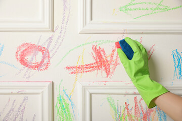Woman erasing child's drawing from white wall, closeup