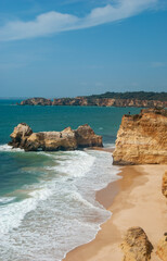 Vertical view of beautiful beach with cliffs and long waves, blue sky with rare clouds, deep blue water - Space for text