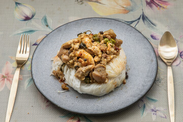 Green curry with chicken (Kaeng kheow hwan with chicken) on top of soft rice noodle on ceramic plate. Authentic Thai food, Selective focus.