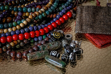 a variety of beads made of natural stones, Tibetan ji beads and metal inserts are randomly scattered on the golden surface next to beautiful red and beige linen bags