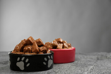 Wet pet food in feeding bowls on grey table. Space for text