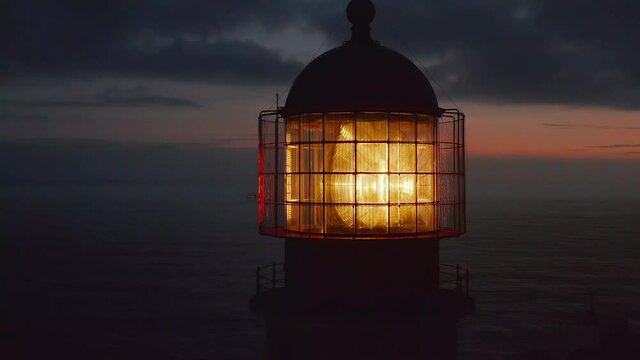 Close up of lighthouse shining head fresnel lens at dusk, drone circling around reveals sensational evening sea panorama, Lagos, Portugal