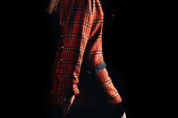 Part of a female figure wearing a checkered red jacket on black background. Runway fashion show