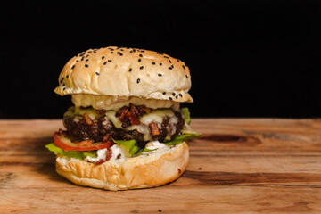 Delicious hamburger on the left on top of a wooden table with black background.