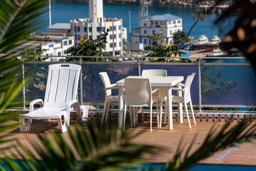 White plastic chairs with table and sun loungers near the pool.
