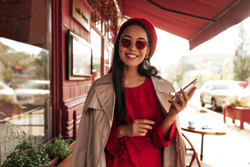 Tanned young brunette woman smiles sincerely in street cafe. Attractive Asian lady in red beret,...