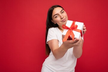 Shot of attractive positive smiling young brunette woman isolated over colourful background wall wearing everyday trendy outfit holding gift box and looking at camera