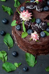 Obraz na płótnie Canvas The most beautiful vegan cake is a birthday cake with blueberries, mint, blackberries and fresh flowers. Organic Chocolate Vegan Cake. Rustic, rustic and homely with love.