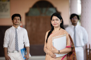 Confident smiling Indian school teacher with students in background