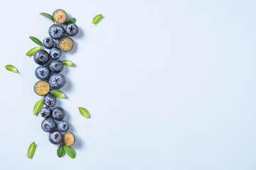 Concept flat lay with a  few juicy blueberries with green leaves on blue background. Top view and copy space