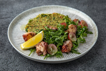 Grilled octopus salad, bulgur with spinach. Ready menu for the restaurant. Neutral gray blue textured background