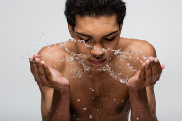 shirtless african american man washing face with fresh water isolated on grey