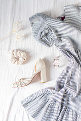 Beauty fashion flat lay with women's dress, a scrunchie, a wrist watch, high heels and a dried flower on white cotton cloth.  Top view fashion blog lifestyle concept