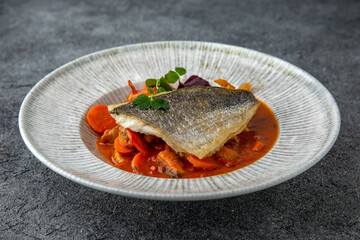 Dorada or sea bass on a pillow of stewed vegetables in sauce. Ready menu for the restaurant. Neutral gray blue textured background