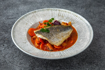 Dorada or sea bass on a pillow of stewed vegetables in sauce. Ready menu for the restaurant. Neutral gray blue textured background