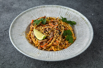 Thai soba with veal vegetables and sesame seeds. Ready menu for the restaurant. Neutral gray blue textured background
