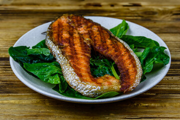 Plate with roasted salmon steak and spinach leaves on a wooden table