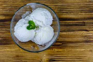 Glass bowl with ice cream balls and mint leaf on a wooden table. Top view