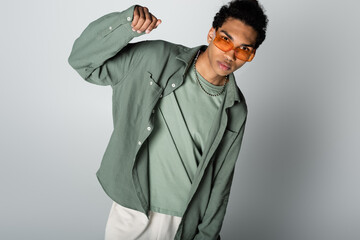 young african american man in stylish clothes and orange eyeglasses posing on grey background