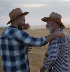 Young farmer with hand on shoulder of elderly farmer talking smiling in field. © Budimir Jevtic