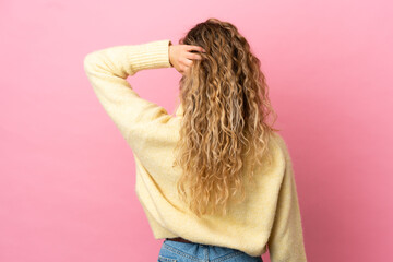Young blonde woman isolated on pink background in back position and thinking