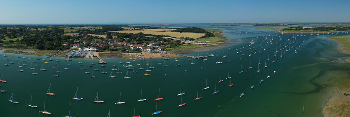 Itchenor West Sussex with sailing boats moored in the estuary and on the wooden jetty set in the beautiful countryside of Southern England. Aerial panoramiv view.