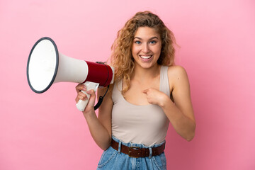 Young blonde woman isolated on pink background holding a megaphone and with surprise facial expression
