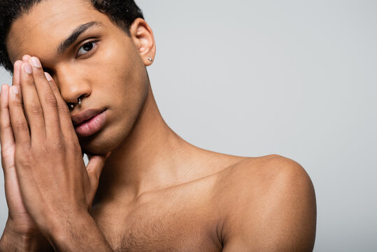 shirtless african american guy with piercing holding hands near face isolated on grey, beauty concept