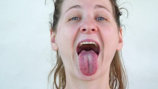 Joke and laugh. Real Caucasian woman smiling and showing tongue. Close-up frame of face on white background. Blue eyes and tousled hair in a ponytail. Happy and cheerful adult girl. raise eyebrows.
