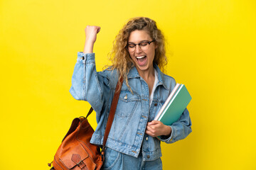 Young student caucasian woman isolated on yellow background celebrating a victory