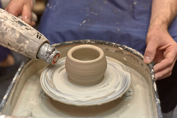 Hands of a man who learns to dry a product on a potter's wheel with a construction hairdryer