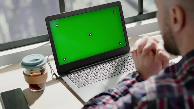 Concentrated bearded guy looks at laptop green screen