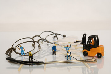 Group of miniature construction workers using a forklift and working power to fix glasses