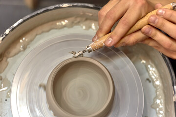Fototapeta premium The hands of the master ceramist with a special tool align the almost finished cup on the potter's wheel