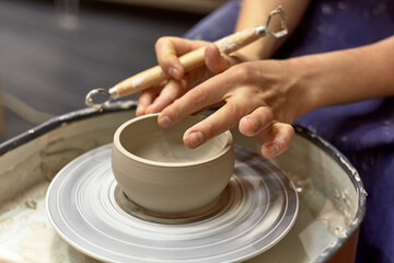 The hands of the master ceramist with a special tool align the almost finished cup on the potter's wheel