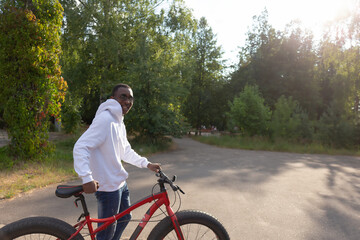 A young happy African-American man with a bicycle in nature
