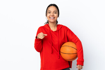 Young woman playing basketball over isolated white background surprised and pointing front