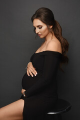 A gorgeous pregnant model girl wearing a black evening dress posing over grey background. Young...
