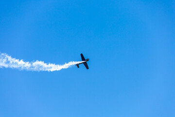 Silhouette airplane stunt fly over clear blue sky. Aerobatic glide with engine smoke behind, power speed transportation. Aviation concept with copy space