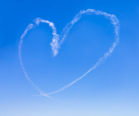 White smoke of heart shape in clear blue sky, imagination of airplane engine trace display with copy space. Symbol of romance, drawing of love floating in the air at omantic moment concept. High angle