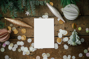 Fototapeta na wymiar Christmas card mock up. Empty greeting card and christmas ornaments, decorations, confetti and pine branches on rustic wooden background. Flat lay. Space for text. Seasons greetings. Template