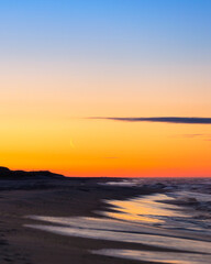 Crescent moon rising just before sunrise over a beach. Jones Beach State Park, New York 