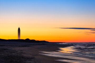 Crescent moon rising just before sunrise next to a tall tower on the beach. Jones Beach State Park, New York