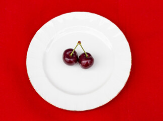 Foto minimalista representando dos cerezas sobre un plato blanco y sobre un fondo rojo