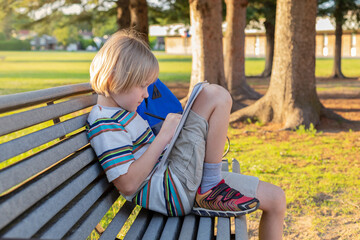 Elementary school student child sitting on bench at schoolyard with backpack, doing homework,...